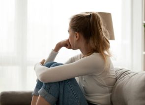 Side view young woman looking away at window sitting on couch at home. Frustrated confused female feels unhappy problem in personal life quarrel break up with boyfriend or unexpected pregnancy concept